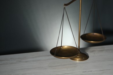 Photo of Scales of justice on light wooden table against gray background, closeup. Space for text