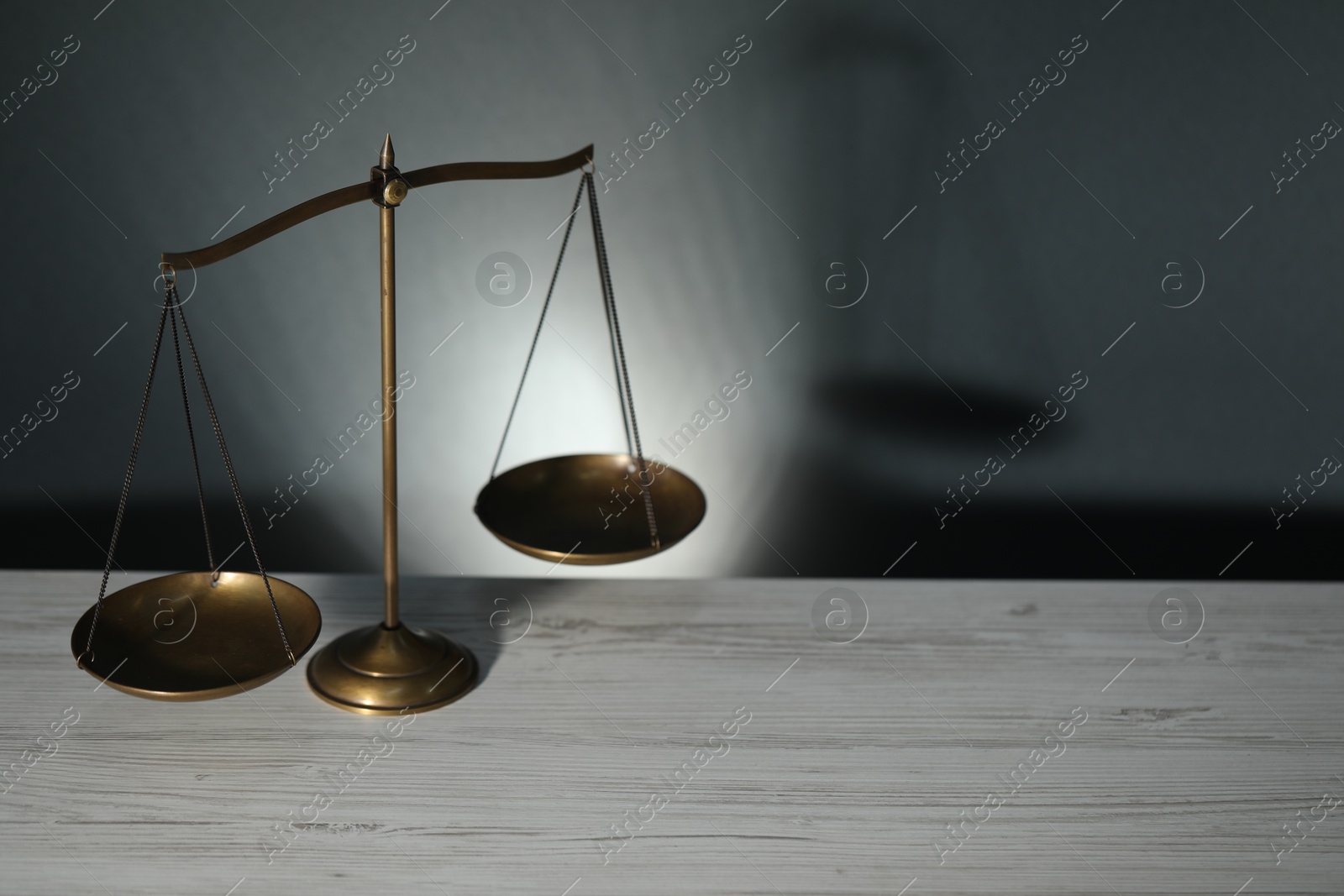 Scales of justice on light wooden table against gray background. Space for text Photo of Scales of justice on light wooden table against gray background. Space for text