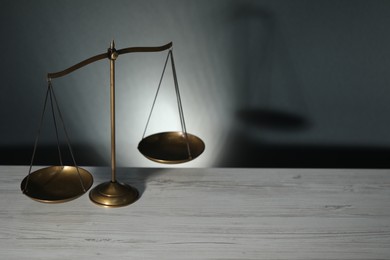 Photo of Scales of justice on light wooden table against gray background. Space for text