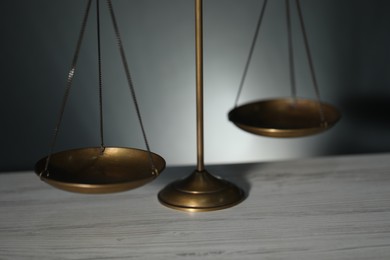 Photo of Scales of justice on light wooden table against gray background, closeup
