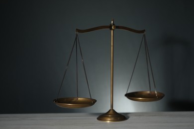 Photo of Scales of justice on light wooden table against gray background