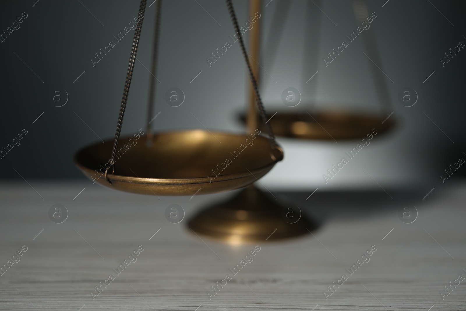 Photo of Scales of justice on light wooden table against gray background, closeup
