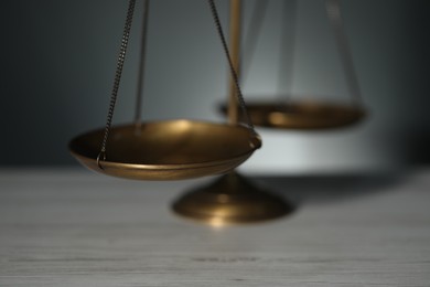 Photo of Scales of justice on light wooden table against gray background, closeup