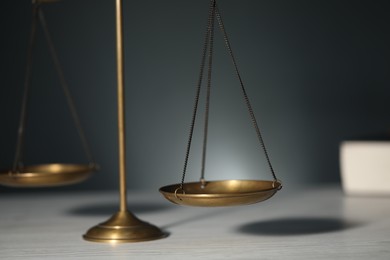 Photo of Scales of justice on light wooden table against gray background, closeup