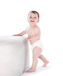 Photo of First steps. Cute little baby in diaper near pouf on white background