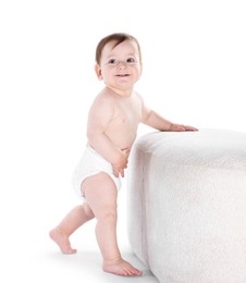 Photo of First steps. Cute little baby in diaper near pouf on white background