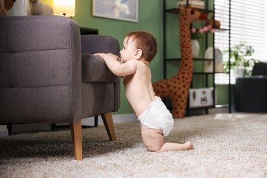 Photo of First steps. Cute little baby in diaper near sofa at home, space for text