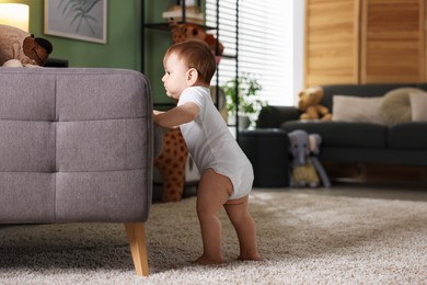 Photo of First steps. Cute little baby near sofa at home, space for text