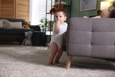 Photo of First steps. Cute little baby near sofa at home, space for text