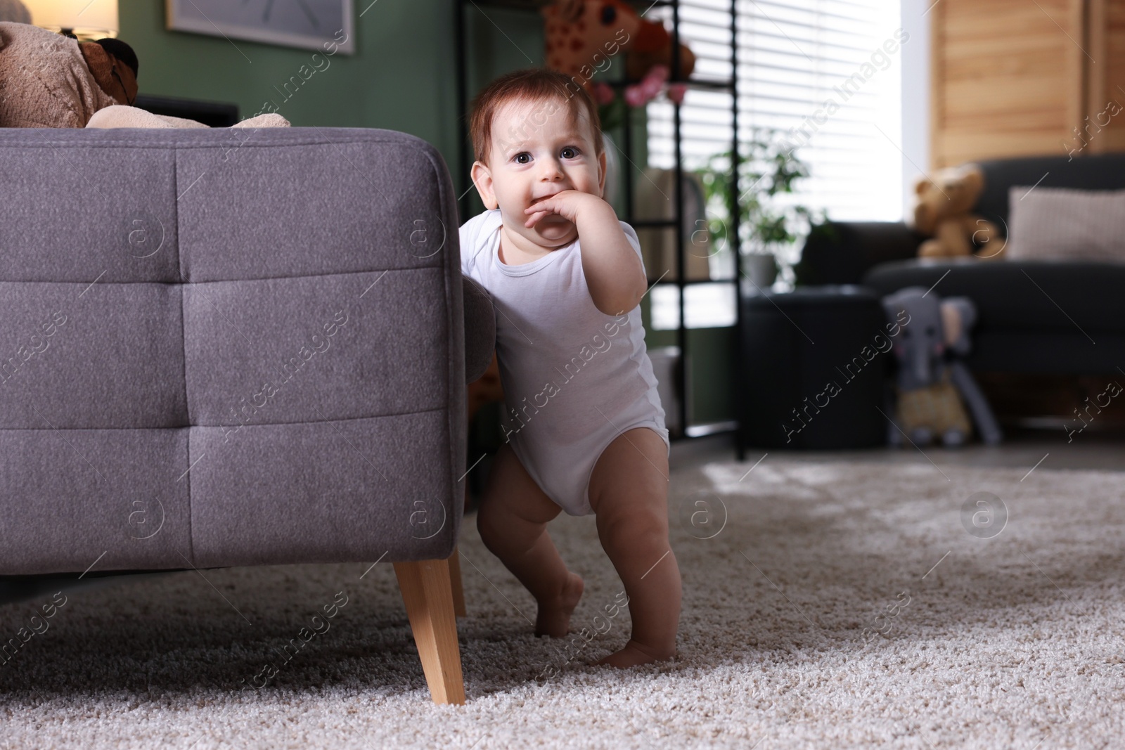 First steps. Cute little baby near sofa at home, space for text Photo of First steps. Cute little baby near sofa at home, space for text