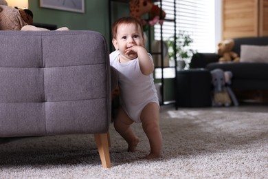 Photo of First steps. Cute little baby near sofa at home, space for text