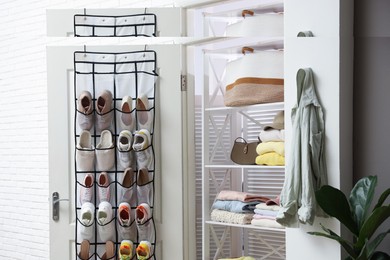 Photo of Organizer with different footwear on door and clothes indoors. Shoe storage