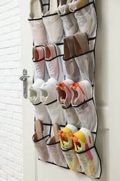 Photo of Organizer with different footwear on door indoors. Shoe storage