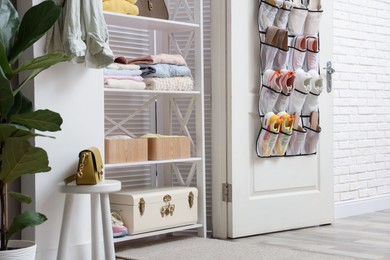 Photo of Organizer with different footwear on door and clothes indoors. Shoe storage