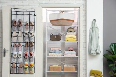 Photo of Organizer with different footwear on door, accessories and clothes indoors. Shoe storage