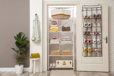 Photo of Organizer with different footwear on door, accessories and clothes indoors. Shoe storage