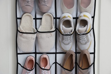 Photo of Organizer with different footwear on door indoors. Shoe storage