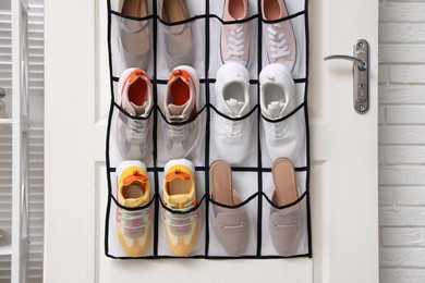 Photo of Organizer with different footwear on door indoors. Shoe storage