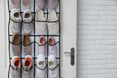 Photo of Organizer with different footwear on door indoors, space for text. Shoe storage