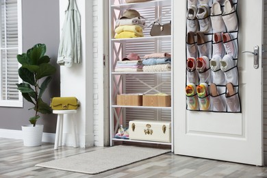 Photo of Organizer with different footwear on door, accessories and clothes indoors. Shoe storage