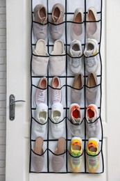 Photo of Organizer with different footwear on door indoors. Shoe storage