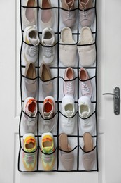 Photo of Organizer with different footwear on door indoors. Shoe storage