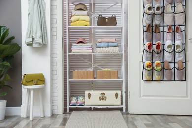 Photo of Organizer with different footwear on door, accessories and clothes indoors. Shoe storage