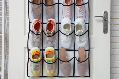 Photo of Organizer with different footwear on door indoors. Shoe storage