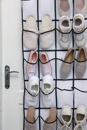 Photo of Organizer with different footwear on door indoors. Shoe storage