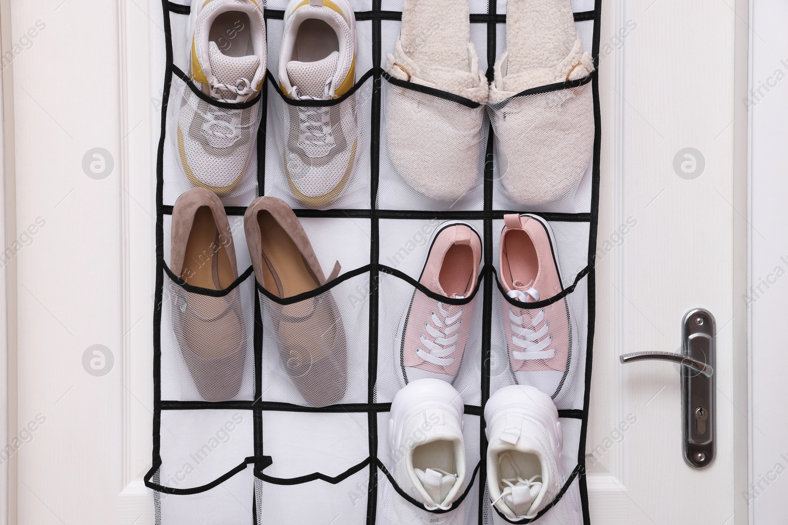 Photo of Organizer with different footwear on door indoors. Shoe storage