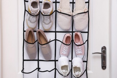 Photo of Organizer with different footwear on door indoors. Shoe storage