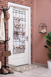 Photo of Organizer with different footwear on door, clothes and houseplant indoors. Shoe storage
