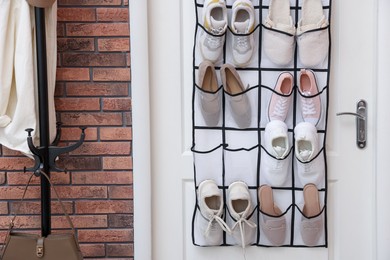 Photo of Organizer with different footwear on door, clothing rack and bag indoors. Shoe storage