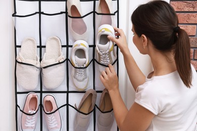 Photo of Woman putting sneaker into organizer at home. Shoe storage