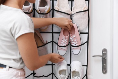 Photo of Woman putting sneakers into organizer at home, closeup. Shoe storage