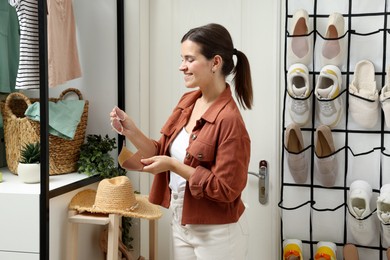 Photo of Woman holding glasses and case near organizer with different footwear at home. Shoe storage