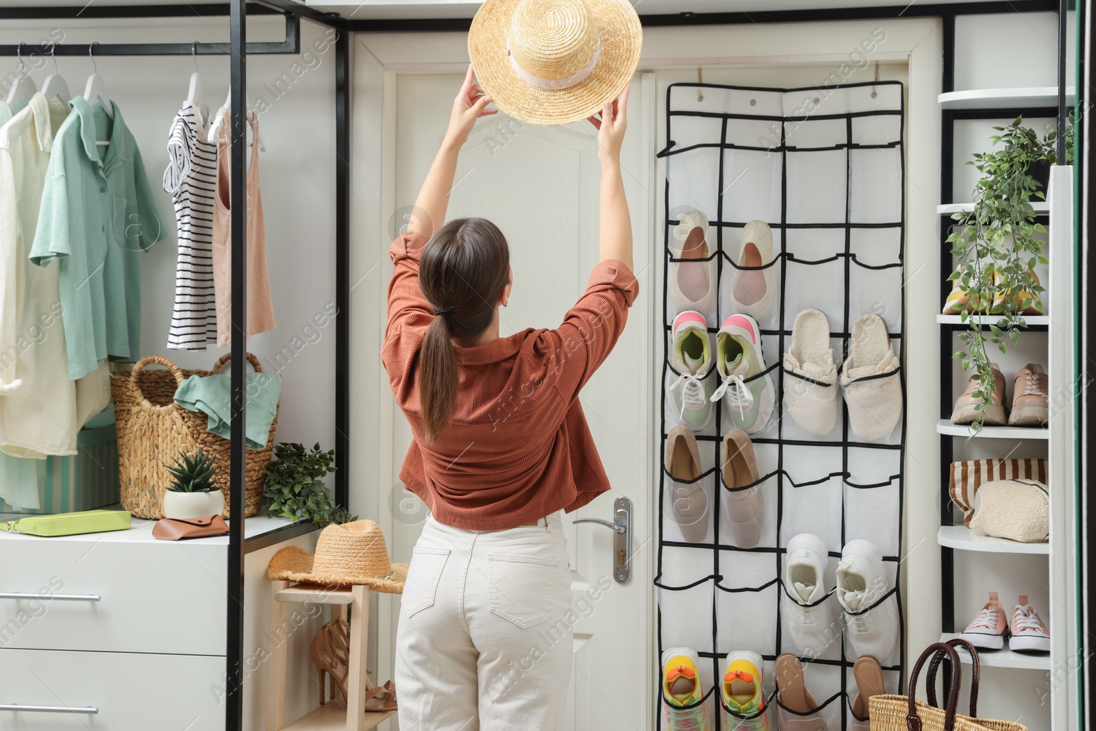 Woman holding straw hat near organizer with different footwear at home, back view. Shoe storage Photo of Woman holding straw hat near organizer with different footwear at home, back view. Shoe storage