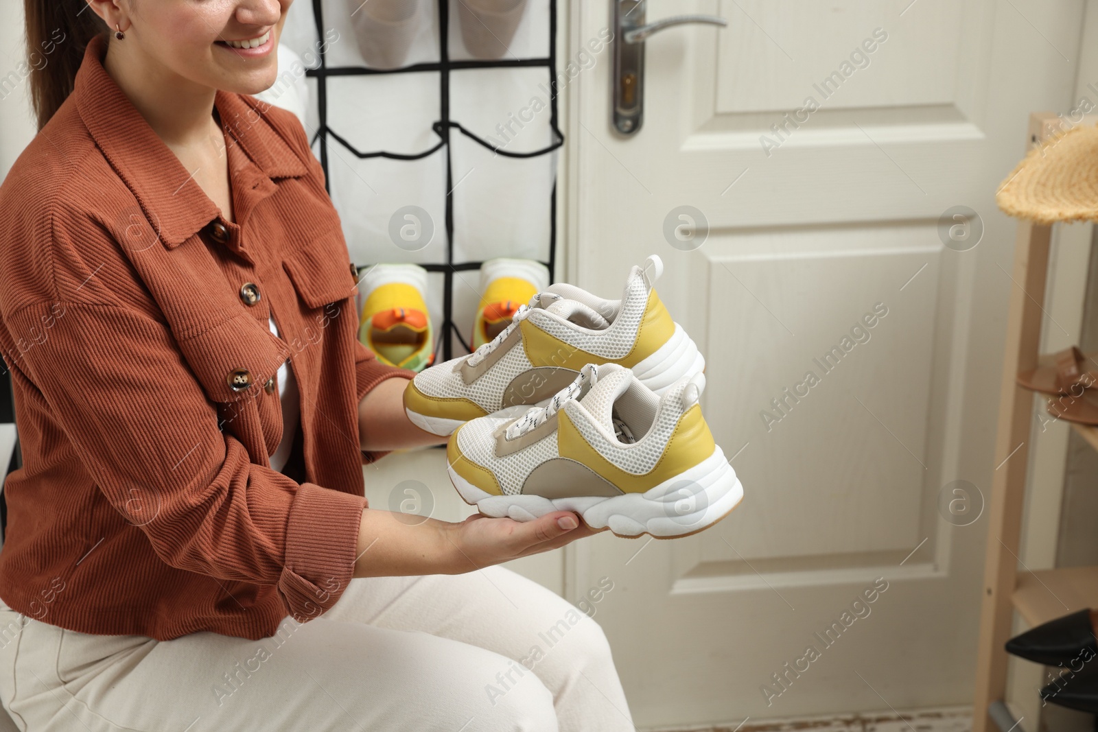 Woman holding sneakers near organizer with footwear at home, closeup. Shoe storage Photo of Woman holding sneakers near organizer with footwear at home, closeup. Shoe storage