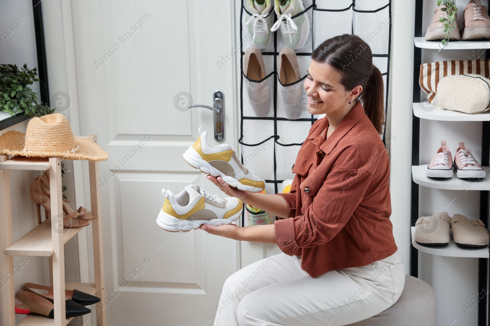 Woman holding sneakers near organizer with different footwear at home. Shoe storage Photo of Woman holding sneakers near organizer with different footwear at home. Shoe storage