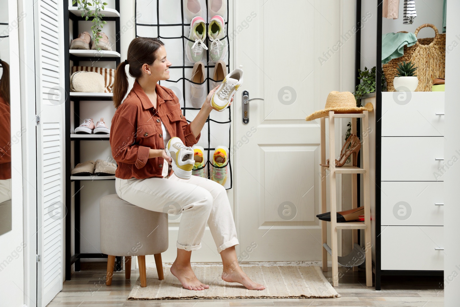 Woman holding sneakers near organizer with different footwear at home. Shoe storage Photo of Woman holding sneakers near organizer with different footwear at home. Shoe storage