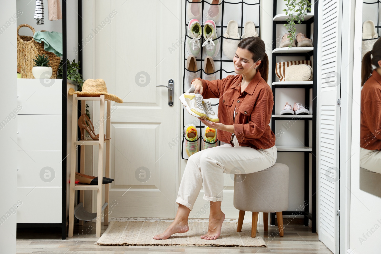 Woman holding sneakers near organizer with different footwear at home. Shoe storage Photo of Woman holding sneakers near organizer with different footwear at home. Shoe storage
