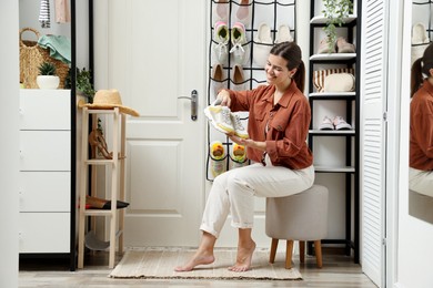 Photo of Woman holding sneakers near organizer with different footwear at home. Shoe storage