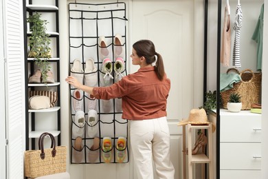 Photo of Woman near organizer with different footwear at home. Shoe storage