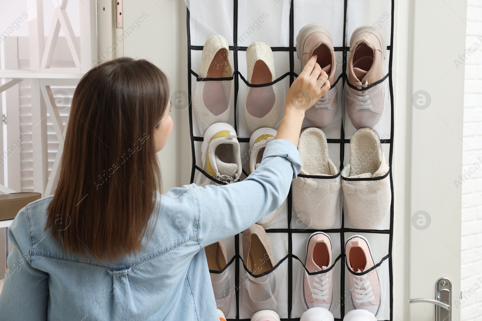 Woman putting sneaker into organizer at home, back view. Shoe storage Photo of Woman putting sneaker into organizer at home, back view. Shoe storage