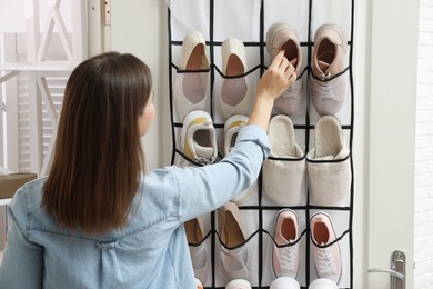 Photo of Woman putting sneaker into organizer at home, back view. Shoe storage