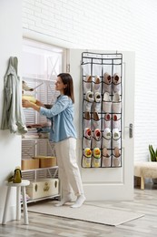 Photo of Woman taking cap from shelf near organizer with different footwear at home. Shoe storage