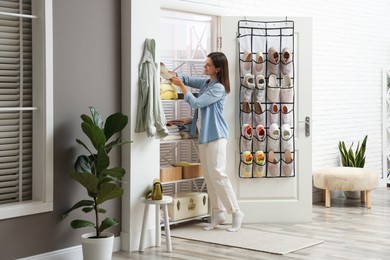 Photo of Woman taking cap from shelf near organizer with different footwear at home. Shoe storage