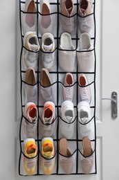 Photo of Organizer with different footwear on door indoors. Shoe storage