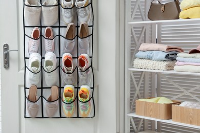 Photo of Organizer with different footwear on door and clothes indoors. Shoe storage