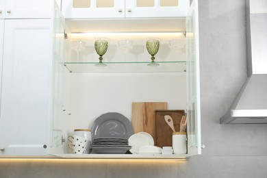 Photo of Clean dishware and glasses on shelves in cabinet indoors